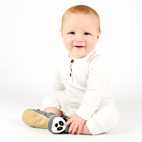 Lächelnder kleiner Junge sitzt auf dem Boden und trägt graue Dotty Fish Schuhe mit weißem und schwarzem Pandamotiv.