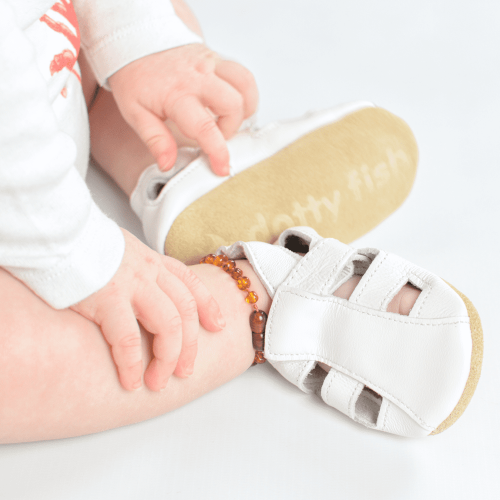 Baby sitzend, mit weißen Dotty Fish Barfußsandalen.