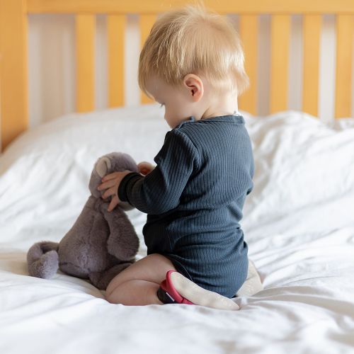 Baby-Junge mit Spielzeug-Affe kniend auf dem Bett, mit roten Dotty Fish Schuhen mit Affenmotiv.