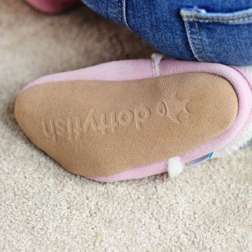 Child wearing Dotty Fish pink suede children's slippers while playing inside 
