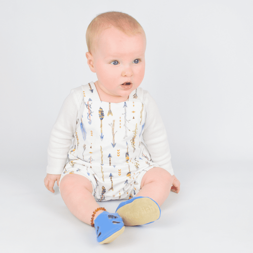 Sitzender kleiner Junge in blauen Dotty Fish Barfußsandalen aus Leder für die ersten Schritte.