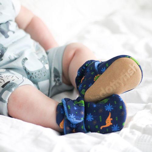 Baby-Junge trägt dunkelblaue Dotty Fish-Schuhe aus Baumwolle mit blauem Fleece-Futter und Dinosaurier-Muster.