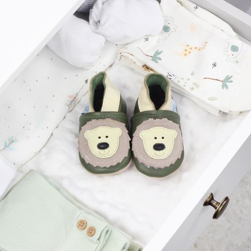Babyschuhe aus Leder mit Bärenmotiv, in einer Schublade mit Babydecken.