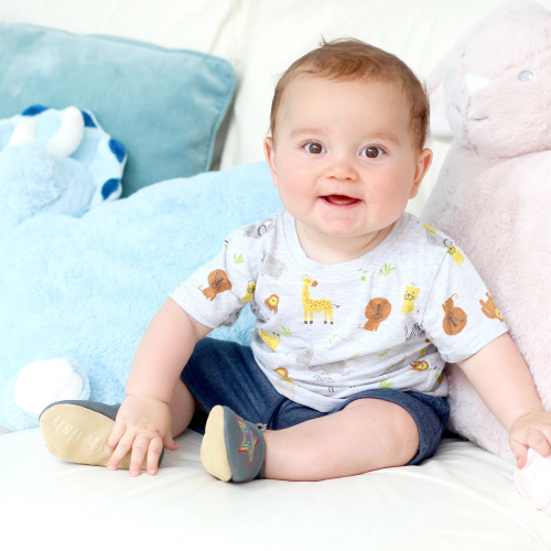 Sitzender kleiner Junge mit grauen Dotty Fish Barfußschuhen mit gesticktem Regenbogenstern.