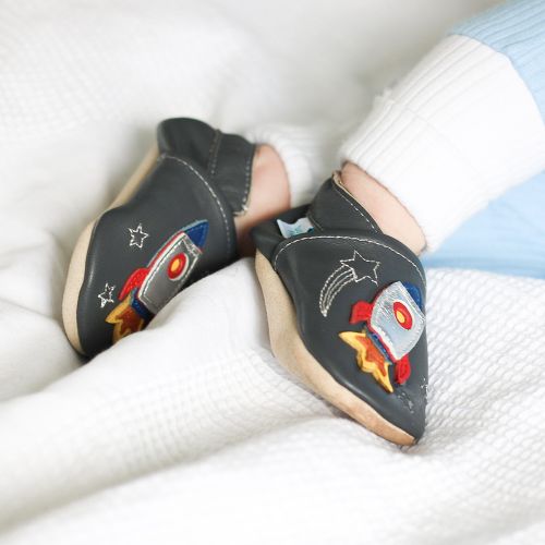 Ein kleiner Junge liegt auf dem Bett und trägt anthrazitfarbene Dotty-Fish-Schuhe mit silbernem Raketendesign.
