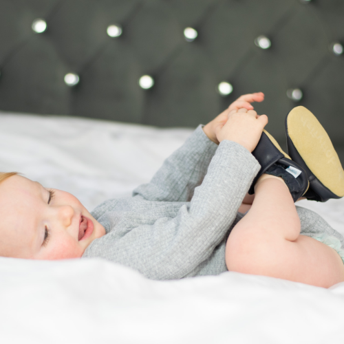 Baby spielt mit seinen Füßen und trägt dabei marineblaue Babyschuhe aus weichem Leder von Dotty Fish 