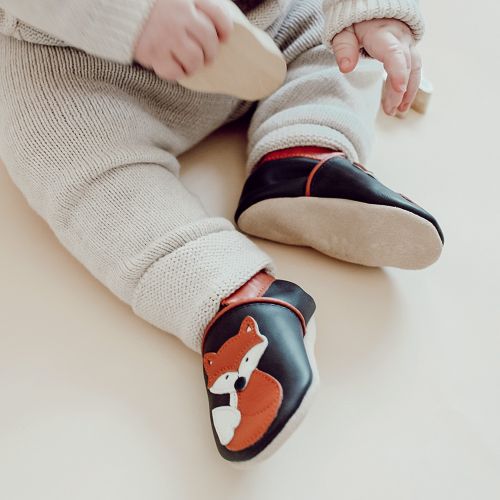 Kleinkind trägt braune Dotty Fish Lauflernschuhe aus Leder mit orangefarbenem und weißem Fuchsmuster.