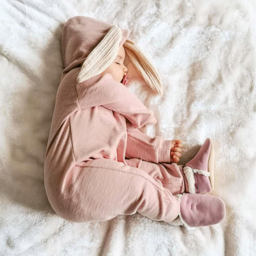 Baby in rosa Wildlederpantoffeln und einem Hasen-Strampelanzug.