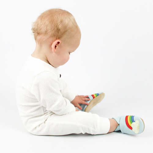 Sitzender Junge mit himmelblauen Dotty Fish Schuhen mit Regenbogen- und Wolkenmotiv.