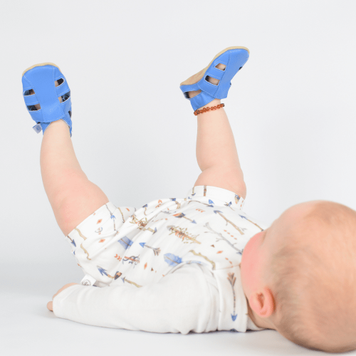 Liegender kleiner Junge mit blauen Dotty Fish Barfußsandalen aus Leder für die ersten Schritte.