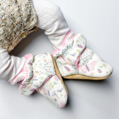 Baby trägt cremefarbene Baumwollstiefel mit Blumenmuster.