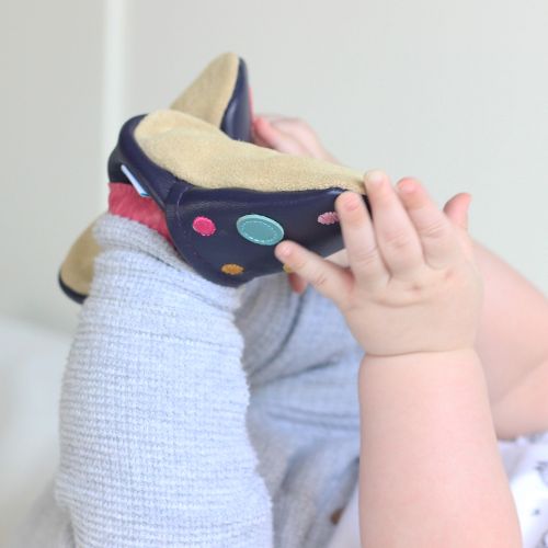 Baby trägt marineblaue Dotty Fish Barfußschuhe mit rosa Knöchelbesatz und bunten Punkten.