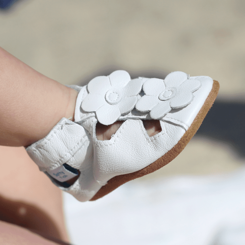 Kleinkind-Mädchen trägt weiße Leder Dotty Fish erste Walker barfuß Sandalen mit weißen Blumen.