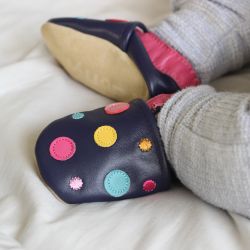 Baby trägt marineblaue Dotty Fish Barfußschuhe mit rosa Knöchelbesatz und bunten Punkten.