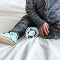 Kleiner Junge sitzt auf dem Bett und trägt mintgrüne Dotty Fish Schuhe mit weißem und schwarzem Pinguinmuster.