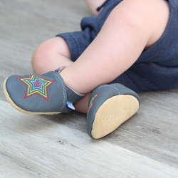 Kleinkind trägt graue Dotty Fish Lauflernschuhe aus Leder mit gesticktem Regenbogenstern.