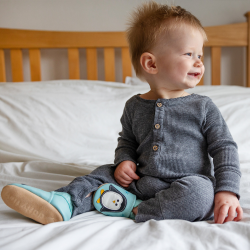 Kleiner Junge sitzt auf dem Bett und trägt mintgrüne Dotty Fish Schuhe mit weißem und schwarzem Pinguinmuster.