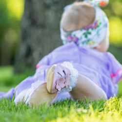 Baby lying on the grass wearing pink leather sandals with flower design from Dotty Fish 
