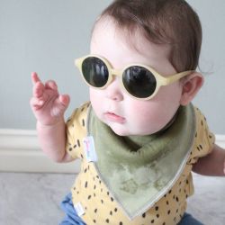 Baby trägt Dotty Fish olivgrünes Baumwolle-Bandana-Lätzchen und Sonnenbrille.