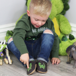 Dotty Fish soft leather baby shoes worn by toddler while playing with dinosaurs
