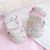 Cream baby booties with floral pattern, sitting on baby blanket.
