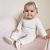 Baby-Mädchen sitzt und trägt weiße Dotty Fish Barfußschuhe mit rosa Knöchelbesatz und rosa Herzen.