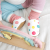 Sitzender Säugling mit weißen Dotty Fish Barfußschuhen mit rosafarbenem Knöchelbesatz und bunten Punkten.